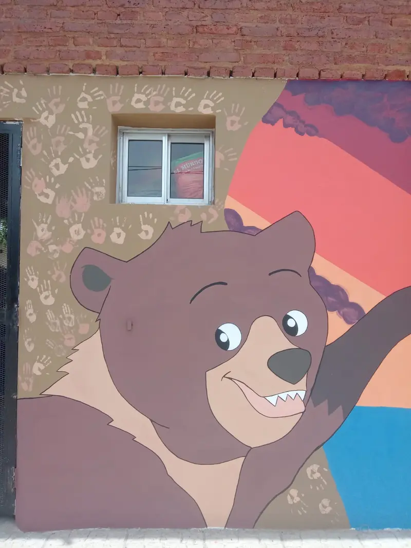 El oso saludando, rodeado de las manitos de los chicos